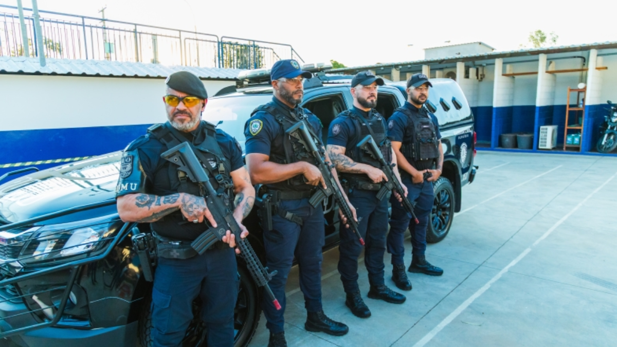 Guarda Municipal em frente a viatura policial, agentes uniformizados com armas em pátio, destacando a oferta de 40 vagas em Paulínia e salário inicial de R$ 4,6 mil.