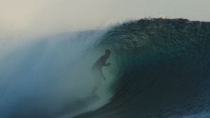 Gabriel Medina em ação dentro de uma onda grande e espumosa, com névoa e luz baixa ao fundo, mostrando o momento de manobra sobre o pico do mar.