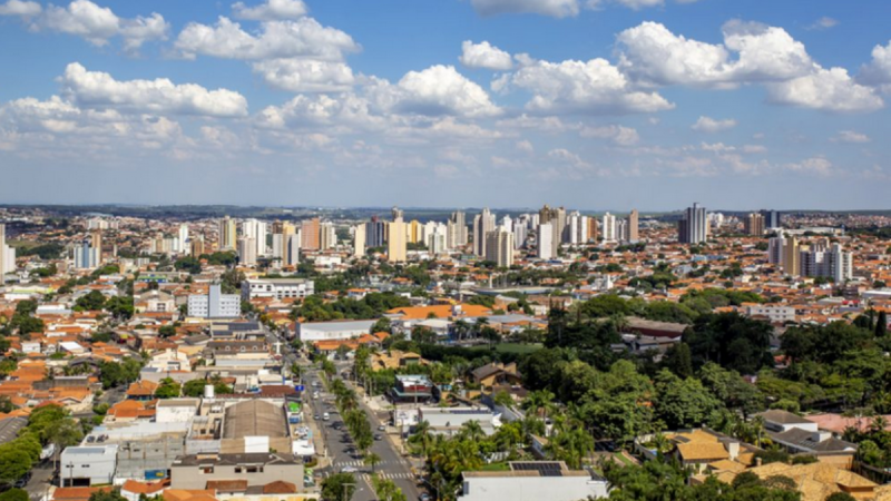 Limeira 200 anos: Vista aérea de Limeira cidade ao fundo com prédios e áreas verdes, céu com nuvens, referência a festas, shows e atrações gratuitas. Confira a programação.