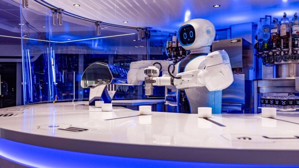 MSC Cruzeiros em Santos: Bar futurista a bordo do MSC Virtuosa com bartender robô humanoide preparando bebidas em um ambiente iluminado em tons de azul e branco.