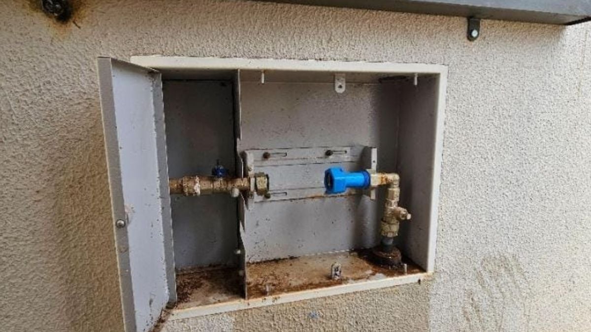Furto de hidrômetros: quadro de medidor de água aberto na parede, com registros e conexões expostos, evidenciando possível violação do hidrômetro em instalação residencial.