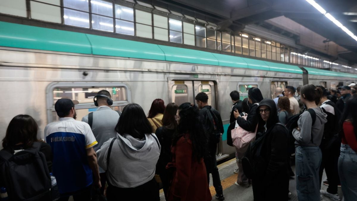 Serviços estaduais feriado de 7 de setembro: Multidão na plataforma de uma estação de trem lotada aguardando a composição passar, com passageiros em fila e iluminação de teto ao fundo, em ambiente urbano de transporte.