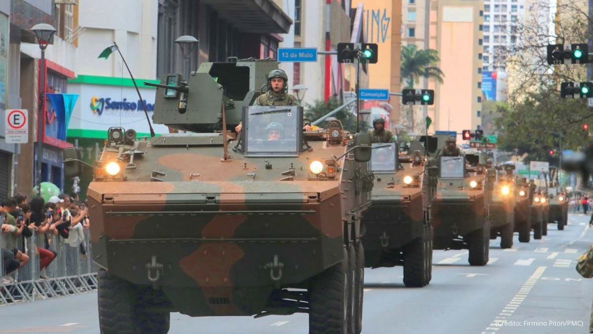 Militares em veículos blindados desfilam em uma avenida durante o 7 de setembro em Campinas, com público nas laterais e sinalização de trânsito ao fundo.