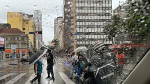 Frente Fria em Campinas: Chuva e ventania em ruas do centro de Campinas, com pessoas usando guarda-chuva e ruas molhadas entre prédios. Cena de clima frio e instável na cidade.