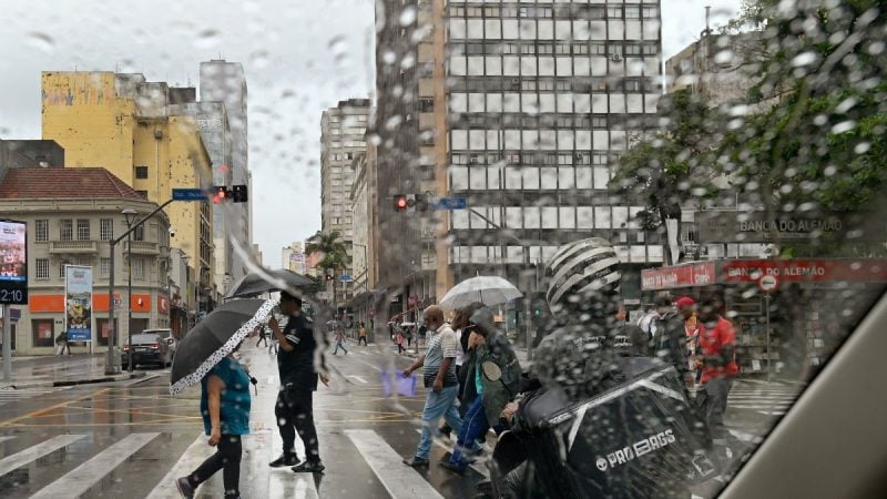 Frente Fria em Campinas: Chuva e ventania em ruas do centro de Campinas, com pessoas usando guarda-chuva e ruas molhadas entre prédios. Cena de clima frio e instável na cidade.