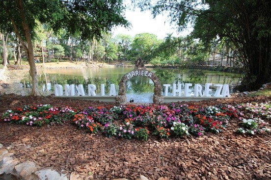 o que fazer em Limeira: Placa com os dizeres “MARIA THEREZA” no Bosque Prefeita Maria Thereza, em Limeira, com jardim de flores e espelho d’água cercado por árvores.