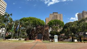 O que fazer em Limeira: vista de um jardim com árvores e um grande prédio ao fundo, em um espaço urbano com entrada pavimentada e sinalização ao lado, ideal para passeio de fim de semana.