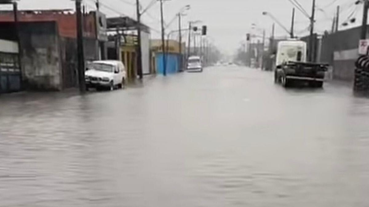 Rua urbana em clima de neblina, com veículos ao longo da via e prédios ao lado, imagem desfocada e atmosférica mostrando carros seguindo pelo caminho.