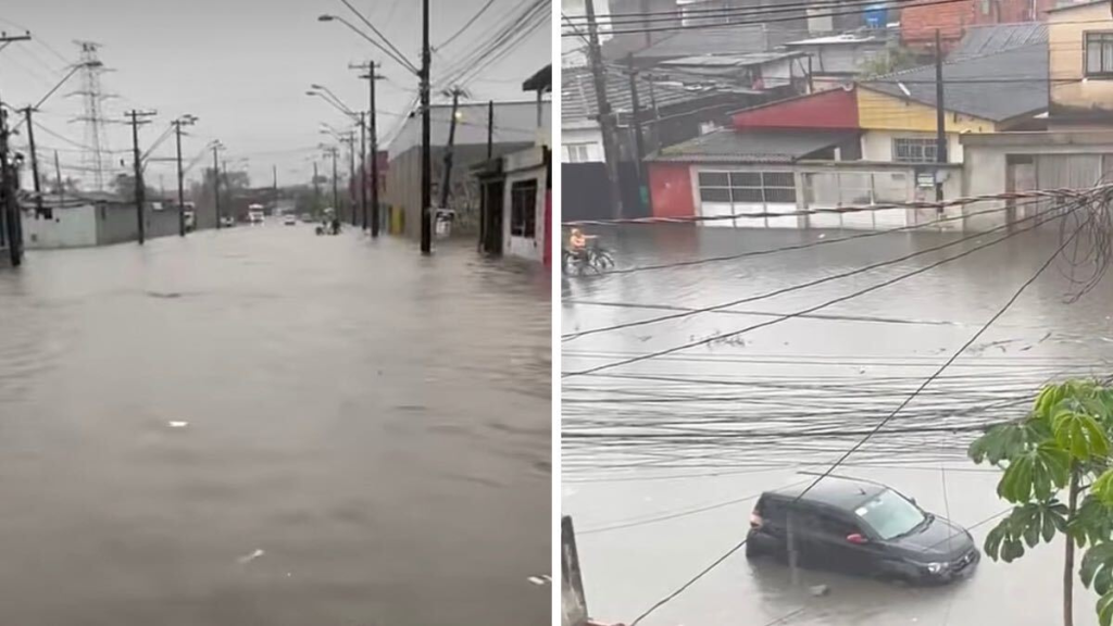 Rua alagada com água cobrindo a pista e carros em área urbana, com postes e fiação elétrica ao fundo durante uma enchente.