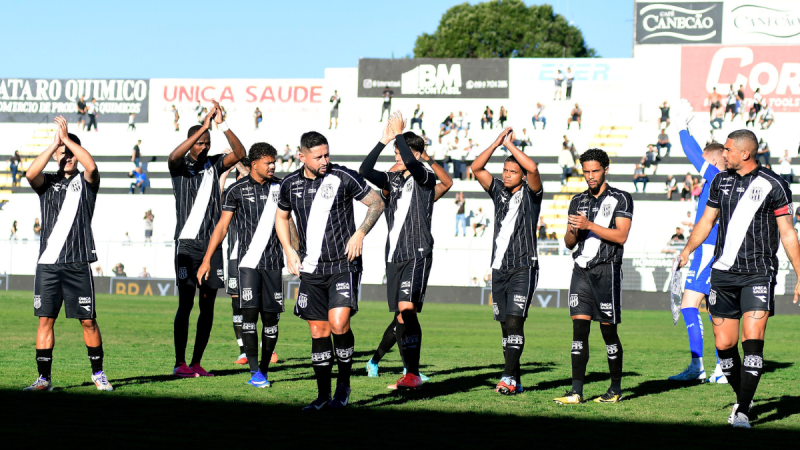 Jogadores do SAF carioca celebram em campo de futebol durante jogo da Ponte, com atletas fazendo gesto de comemoração em estádio ao fundo, Ponte SAF Boavista.