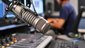 Microfone profissional em estúdio de rádio com locutor ao fundo, reforçando o streaming de rádio durante a propaganda eleitoral e ampliando a audiência.