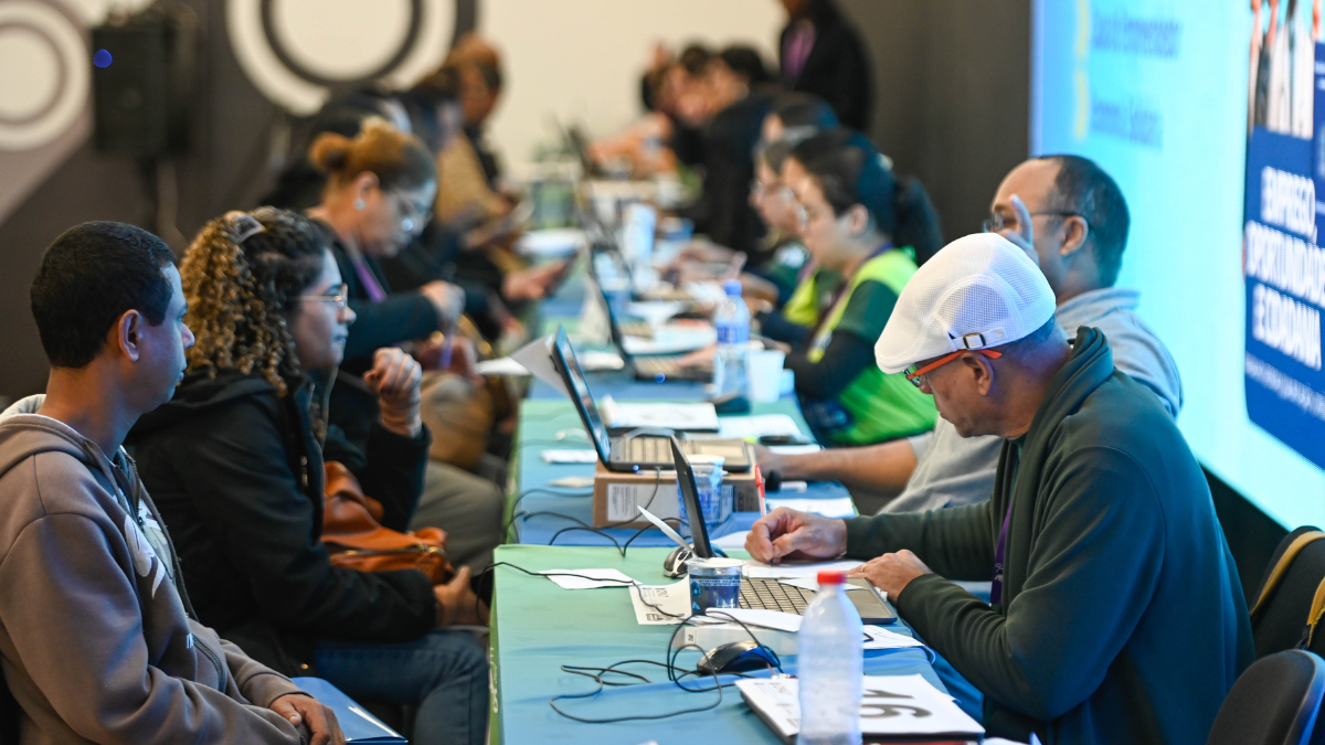 feirão de emprego em Campinas com candidatos reunidos em mesas durante entrevistas e triagem de vagas, em evento de recrutamento profissional, com cartazes ao fundo.