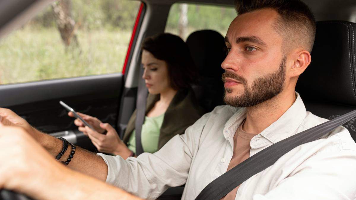 Homem dirigindo um carro, com uma jovem no banco de trás usando o celular durante uma viagem, tema sobre Uber e possibilidade de vídeo ao vivo em deslocamentos