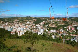 Vista do Teleferico em Serra Negra, com cabines suspensas sobre a cidade e morros verdes ao fundo sob céu azul com nuvens.