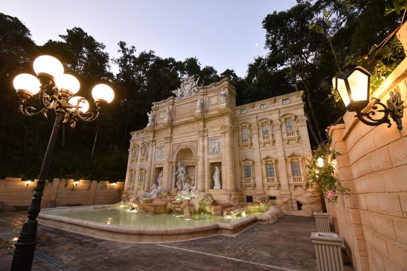 Fontana Di Trevi em Serra Negra: vista noturna da fonte histórica com luzes decorativas, estátuas e jardim ao redor em ambiente urbano arborizado.