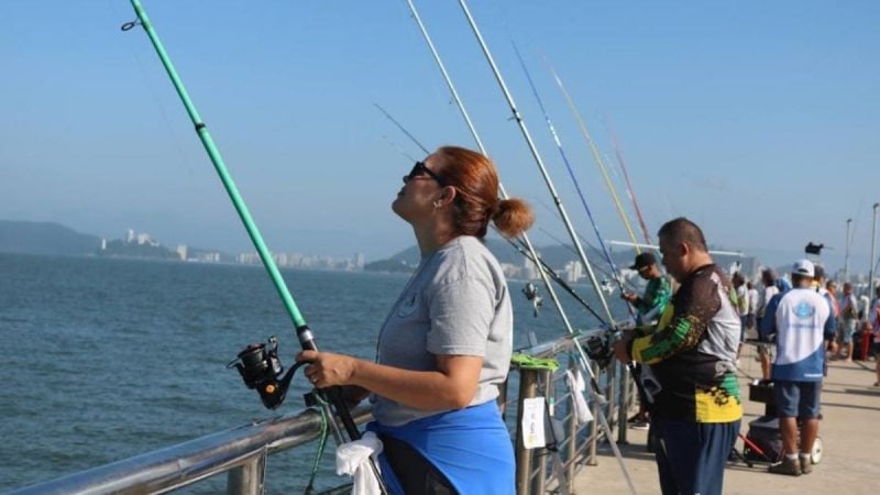 Pessoas pescando em barco ao longo da orla, com varas de pesca e mar ao fundo; Santos reconhece Pesca artesanal como Patrimônio Cultural Imaterial.