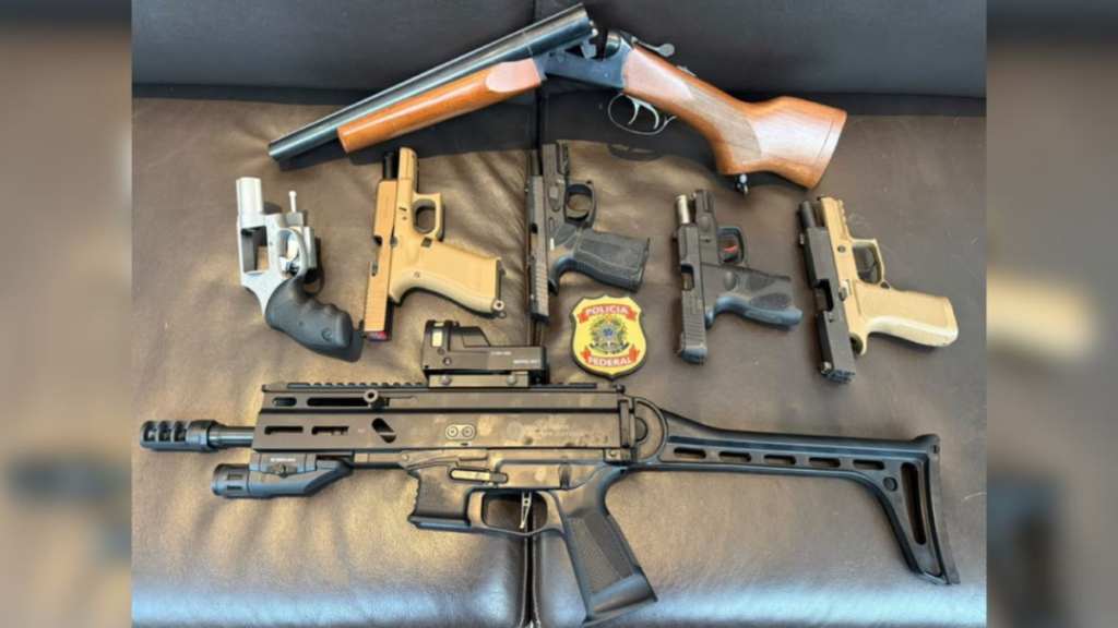 filme sobre Bolsonaro: Foto mostra sete armas de fogo apreendidas em operação, incluindo pistolas e carabinas sobre superfície, com escudos e itens de segurança ao centro. Divulgação/PF.