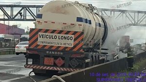 Veículo longo da Randon em área industrial, com placa “VEÍCULO LONGO” e composição de transporte; ao fundo há estruturas metálicas e caminhões.