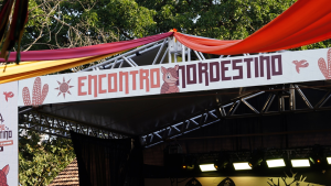 Encontro Nordestino de Piracicaba: lona de palanque com banner “Encontro Nordeste” e estrutura de palco montada no Engenho Central, com barracas e vegetação ao fundo.