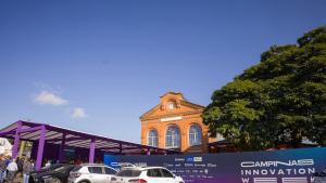 Vista externa do evento Campinas Innovation Week no Pátio Ferroviário, destacando o prédio histórico de tijolos ao fundo, a estrutura roxa à esquerda e o painel do evento à frente.