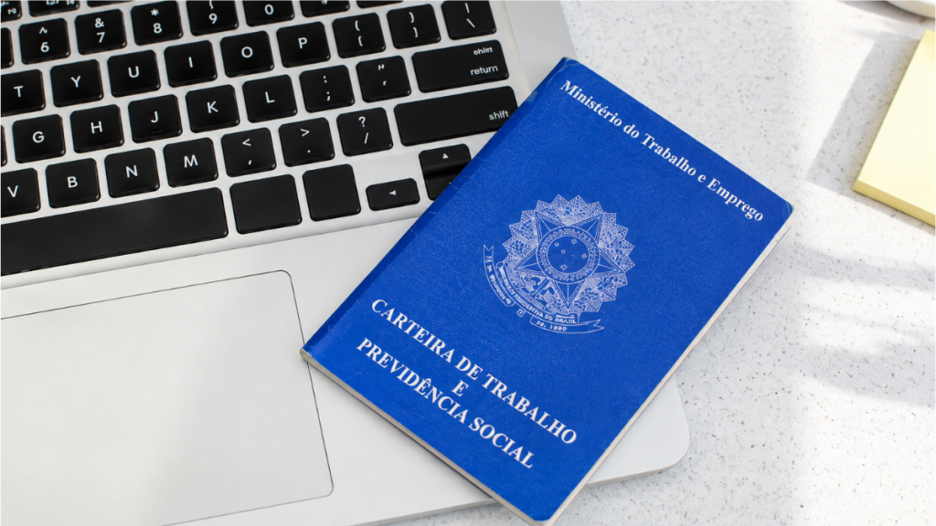 Carteira de Trabalho e Previdência Social azul sobre teclado de computador, com o texto “Ministério do Trabalho e Emprego” visível.