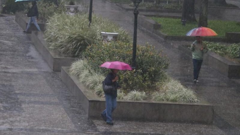 Chuva forte em Santos, com pessoas caminhando em meio a grande volume de água e guarda-chuvas durante o período que registrou 203,1 mm de chuva em nove dias.