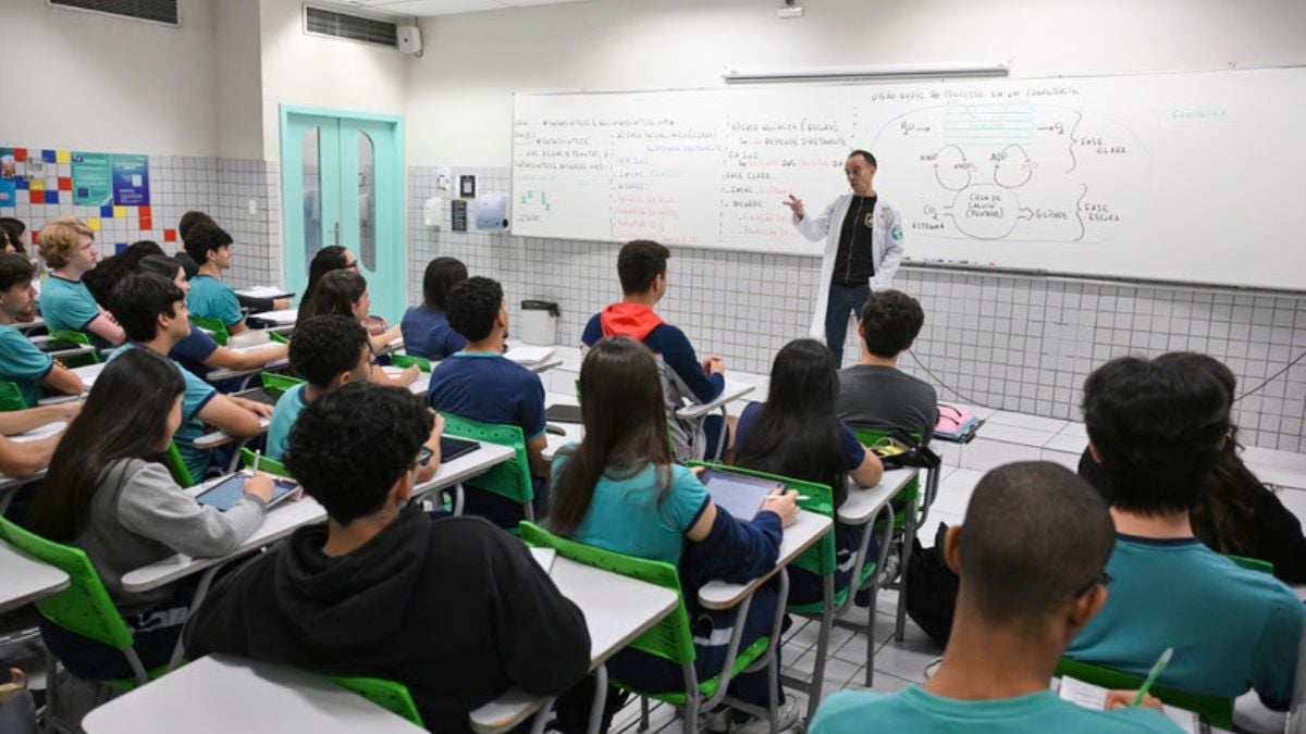 Sala de aula com estudantes em carteiras e professor escrevendo no quadro, com turma estudando para o Enem 2026 e revisando conteúdos.