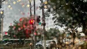 Campinas em horário de fim de tarde com carros na via, semáforos e luzes refletidas em chuva, com partículas luminosas na cena e árvores ao lado da rua.