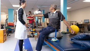 Desafio Teleton com profissional e paciente em clínica de reabilitação, realizando exercícios físicos em ambiente com equipamentos e bola terapêutica; veja a evolução das doações à AACD por ano.