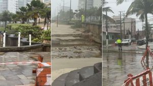 Cratera em Praia Grande vista no calçadão com água e buracos na pista, isolada com barreiras e cones, em meio a moradores e chuva; ao fundo, prédios e palmeiras.