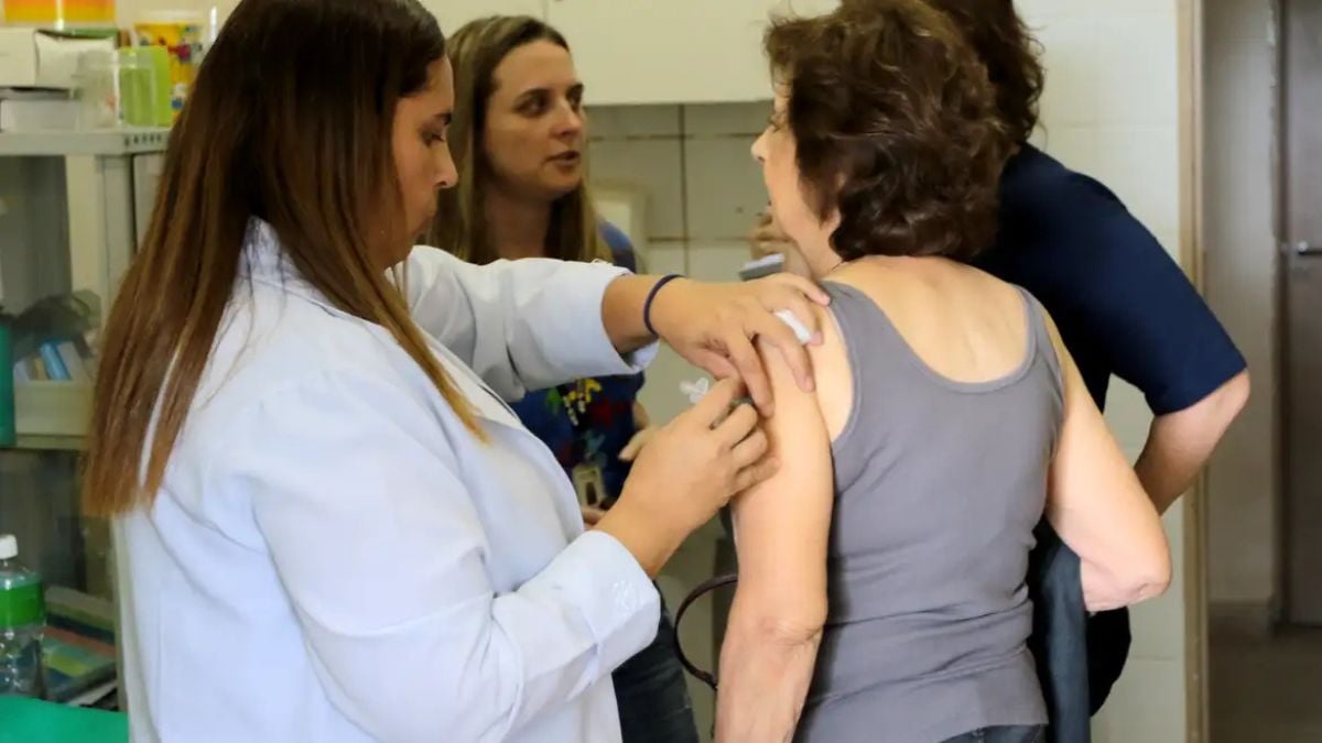 Profissional de saúde aplica vacina no braço de uma idosa em ambiente de atendimento, com foco na imunização do público 85+; SUS libera nova vacina pneumo20. Foto: Wilson Dias / Agência Brasil.