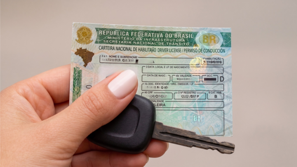 Mão segurando uma carteira nacional de habilitação (CNH) brasileira com chave do carro, mostrando dados e campos de identificação no documento.