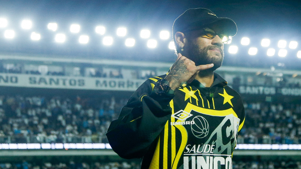 Kerolay Chaves aparece em foto no estádio, em meio à torcida, fazendo gesto de apontar com a mão enquanto veste uniforme com cores preto e amarelo, em clima de jogo do Santos FC. Foto: Raul Baretta.