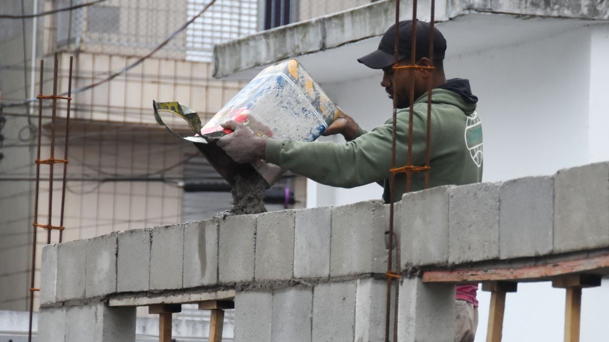 vagas de emprego em Praia Grande: Trabalhador em obra carregando materiais ao lado de um prédio em construção, com ambiente urbano que representa oportunidades locais. Praia Grande abre 128 vagas de emprego no PAT.