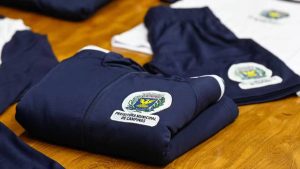 Uniformes escolares dobrados com a identificação “Prefeitura Municipal de Campinas” em destaque, em meio a peças sobre uma mesa, relacionados a apuração às margens da Rodovia dos Bandeirantes.