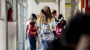 Pessoas caminhando em corredor de instituição de ensino, com mochilas e alunos ao fundo, reforçando a abertura de vagas do Centro Paula Souza para ensino médio, técnico e graduação.
