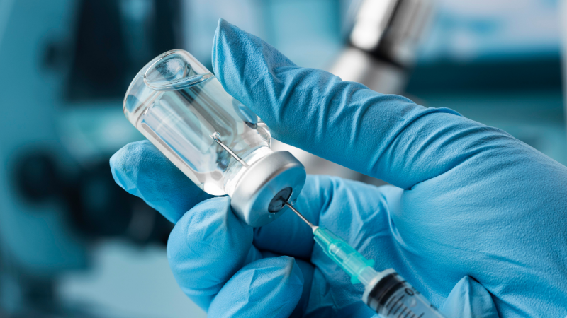 Profissional de saúde preparando dose da vacina Pneumo 20, inserindo uma seringa no frasco de ampola.