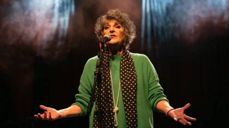 Orquestra Sinfônica da Unicamp: Fátima Guedes em apresentação ao vivo no palco, com microfone e expressão de emoção, ao lado de fundo desfocado em evento em Campinas.