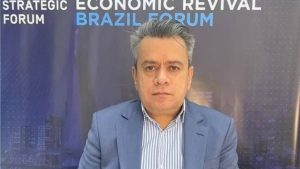 Ex-presidente da SPTrans em foto durante entrevista em evento, com expressão séria e terno azul, ao fundo com banner “Strategic Economic Revival Forum” e “Brazil Forum”.