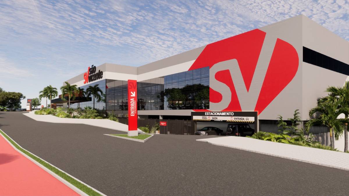 Vista externa de um prédio comercial moderno com fachada branca e grande logotipo vermelho “SV”, área de estacionamento, caminho com faixa vermelha e entrada sinalizada, em ambiente urbano.