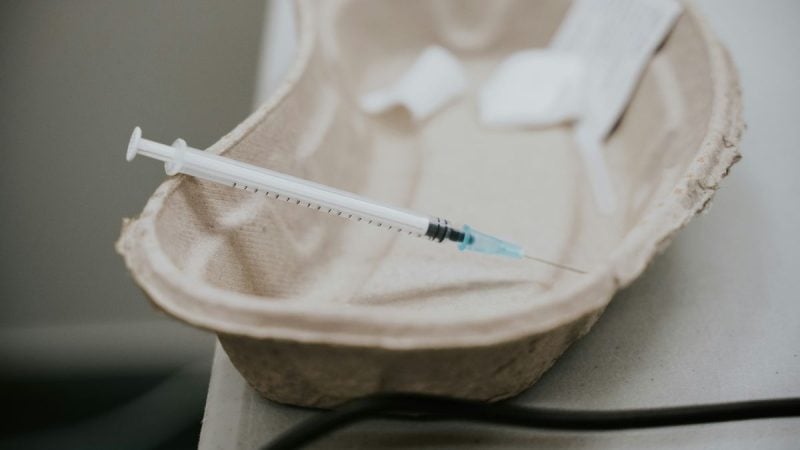 Seringa com agulha aplicada sobre uma bancada, enquanto luvas médicas e estetoscópio aparecem ao fundo, sugerindo preparo para injeção preventiva contra HIV no Brasil. Foto: unsplash.