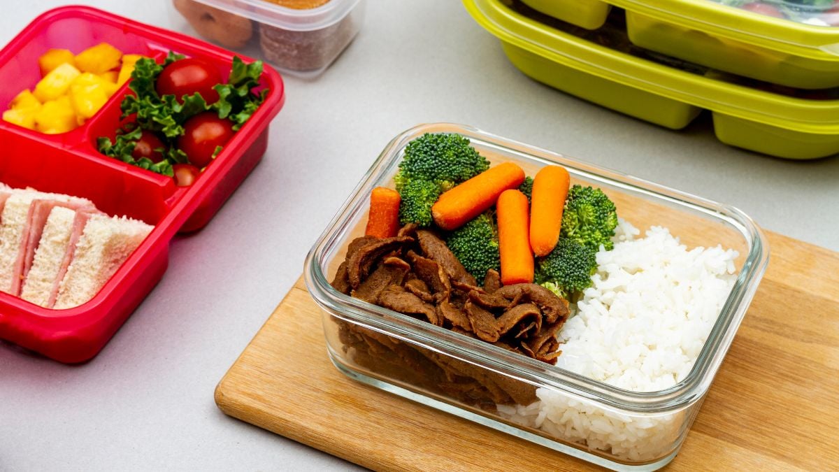 Marmita de almoço pronta em pote de vidro com arroz, carne e legumes como brócolis e cenoura, ao lado de outras marmitas e recipientes na bancada, ideal para organizar a semana.