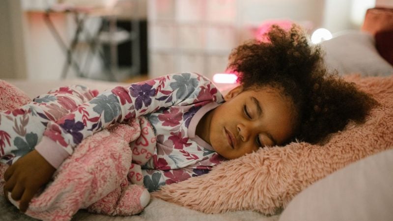 Criança dormindo em um travesseiro macio, com roupa estampada, em um ambiente aconchegante de quarto; conteúdo sobre sono infantil e quando procurar ajuda. Foto: Canva.