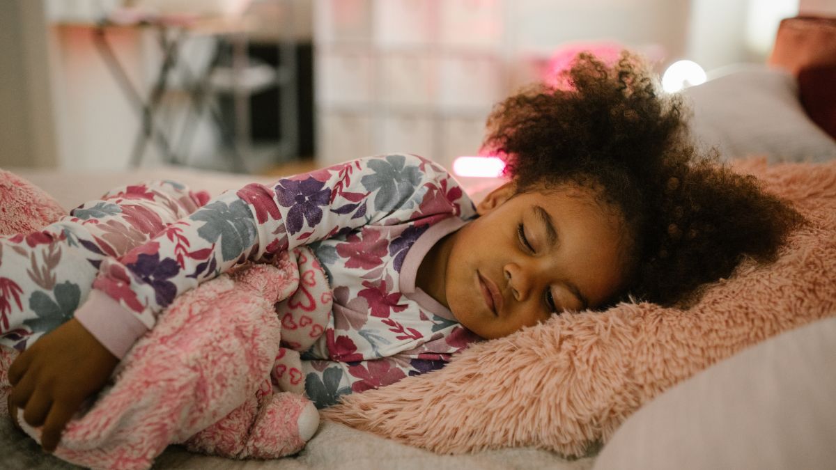 Criança dormindo em um travesseiro macio, com roupa estampada, em um ambiente aconchegante de quarto; conteúdo sobre sono infantil e quando procurar ajuda. Foto: Canva.