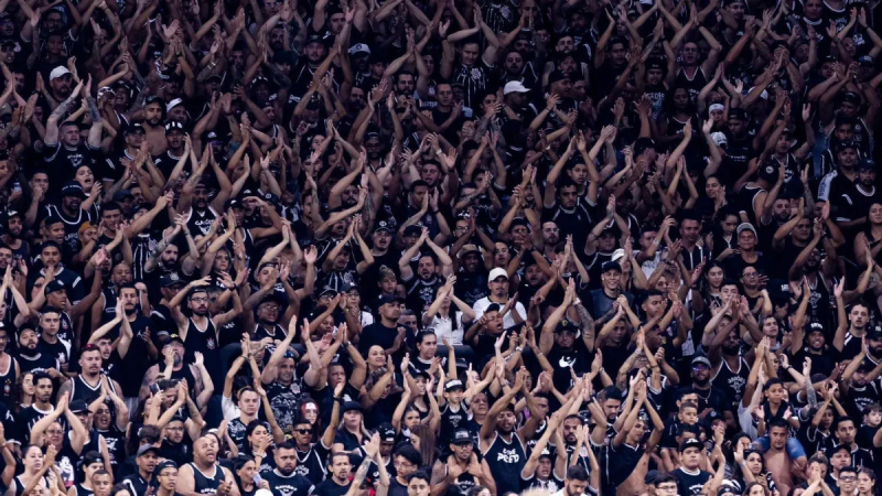 torcida organizada do corinthians com muita gente em estádio, fazendo sinal de mãos e vibrando, indo ao CT cobrar elenco após queda na Libertadores