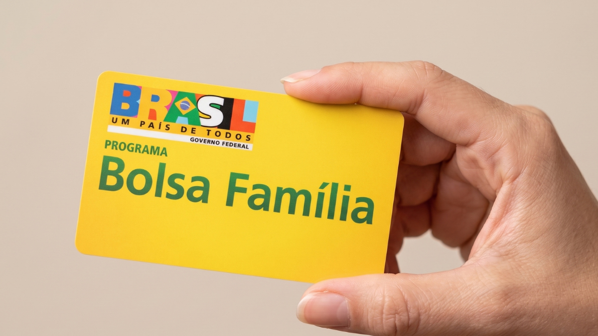 Pessoa segurando um cartão amarelo do programa Bolsa Família (BRASIL, uma país de todos e Governo Federal) com destaque para “Bolsa Família”, em fundo liso claro.