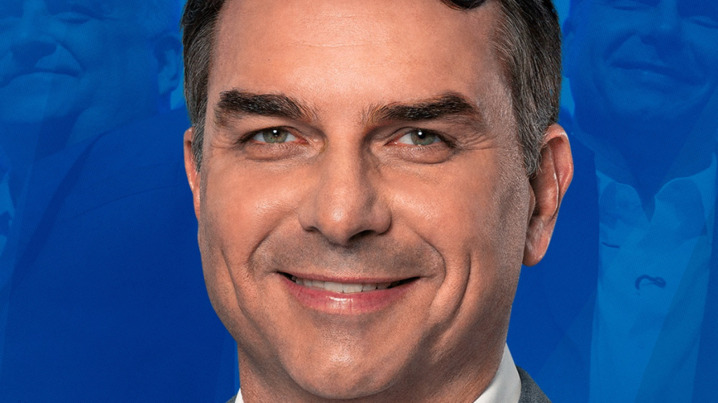 Retrato em plano aproximado (close-up) de Flávio Bolsonaro a sorrir, com um fundo azul onde se vislumbram, de forma subtil, outras imagens em sobreposição.