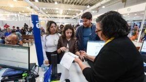 Atendimento em agência com pessoas em fila e funcionários analisando documentos e formulários para emissão de identidade provisória para viagem ao Mercosul, em Campinas.