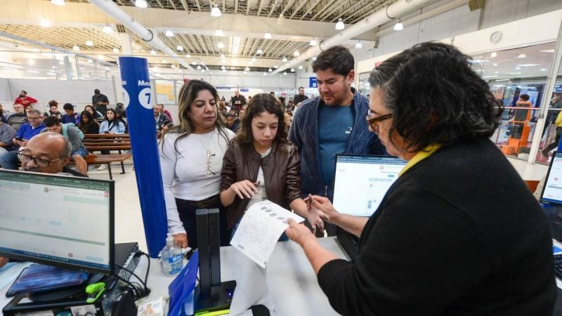 Atendimento em agência com pessoas em fila e funcionários analisando documentos e formulários para emissão de identidade provisória para viagem ao Mercosul, em Campinas.