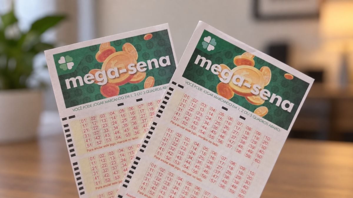 Bilhetes de loteria com o texto Mega-Sena, com cartões verdes e numeração em tabelas coloridas, apoiados em uma mesa em ambiente interno